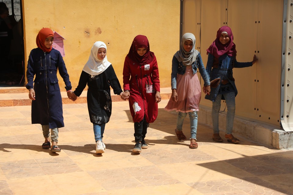 Fem jenter går i en skolegård. Tre av dem holder hender.