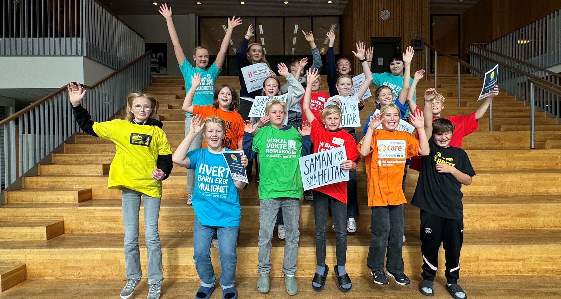 En gruppe barn med t-skjorter fra forskjellige TV-aksjoner hopper og jubler i en trapp.