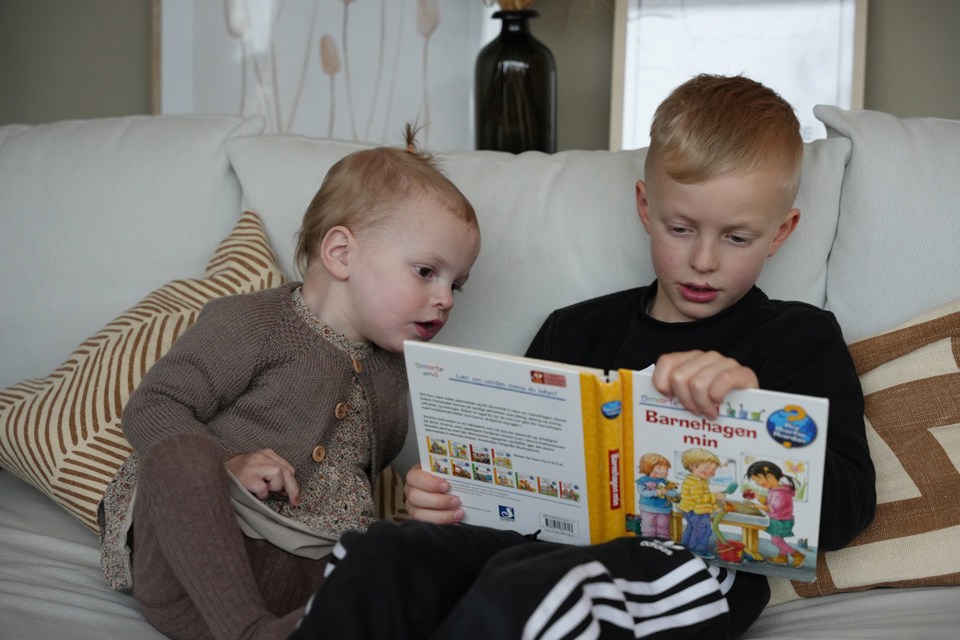 To barn sitter i en sofa og leser en bok.