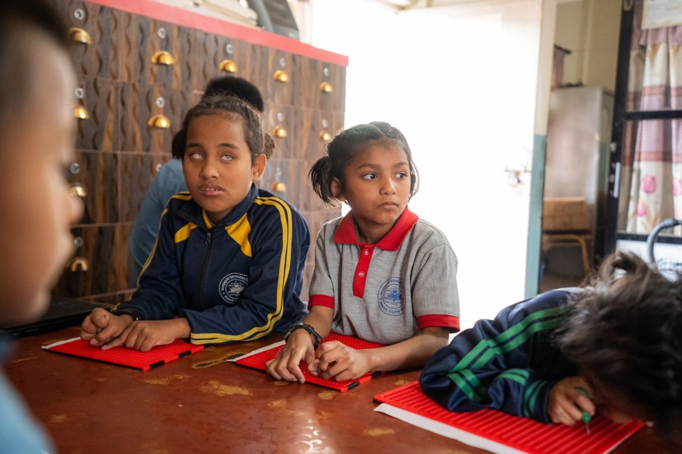 Blinde elever sitter i et klasserom med læreutstyr foran seg. 