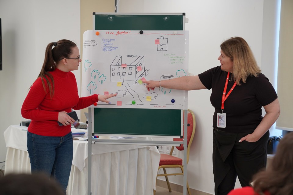 To kvinner viser frem en illustrasjon av en trygg skole i Ukraina.