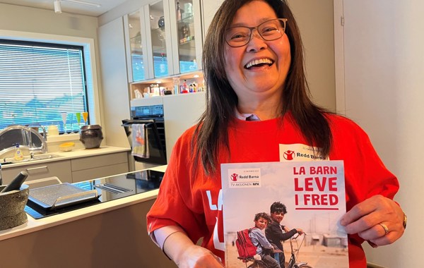 En kvinne med briller har på seg t-skjorte, og viser plakat, fra årets TV-aksjon.