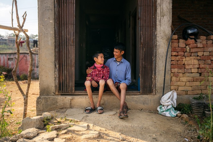 To gutter sitter i en døråpning og holder rundt hverandre i Nepal. Knærne er svellet opp. De smiler. 