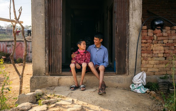 To gutter sitter i en døråpning og holder rundt hverandre i Nepal. Knærne er svellet opp. De smiler. 
