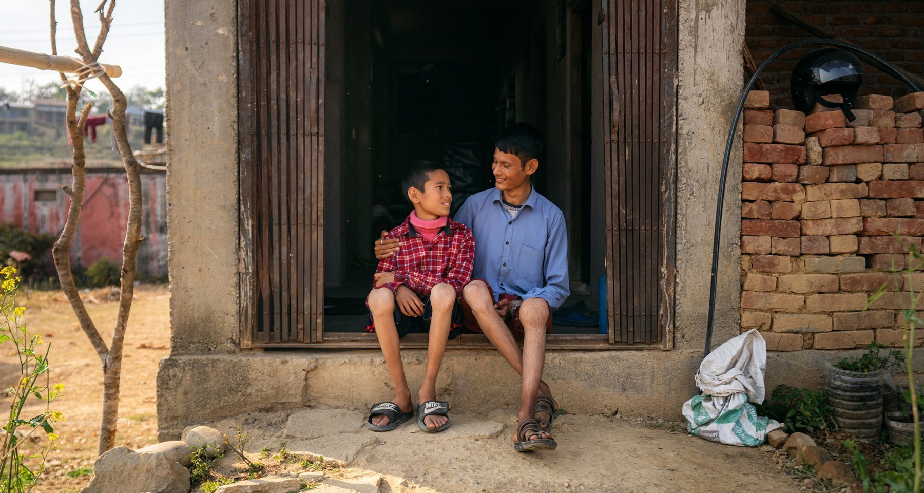 To gutter sitter i en døråpning og holder rundt hverandre i Nepal. Knærne er svellet opp. De smiler. 