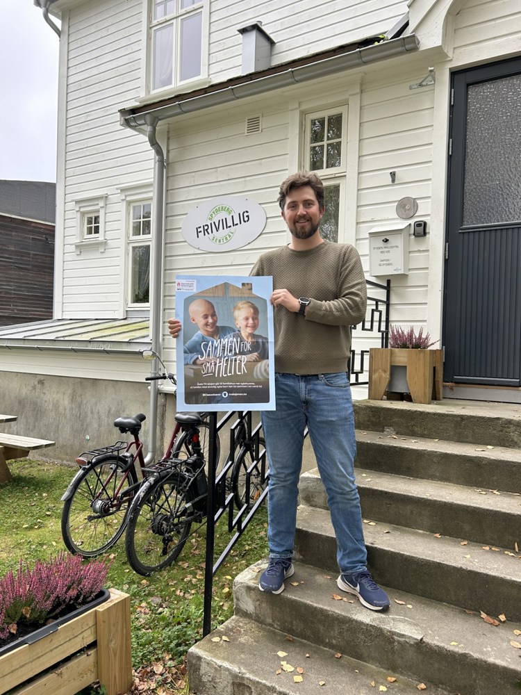 Mann står på utsiden av en frivilligsentral med en TV-aksjonsplakat i hånda