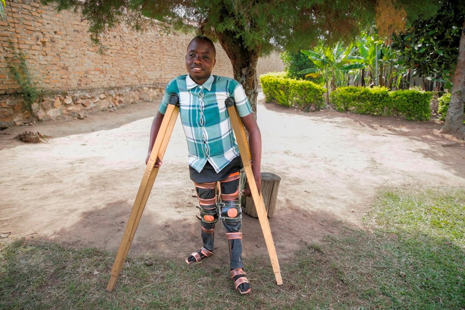 Gutt står under et tre med krykker og smiler.