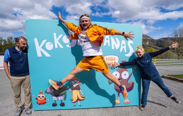 En mann hopper foran et skilt, holdt oppe av en kvinne og en mann.