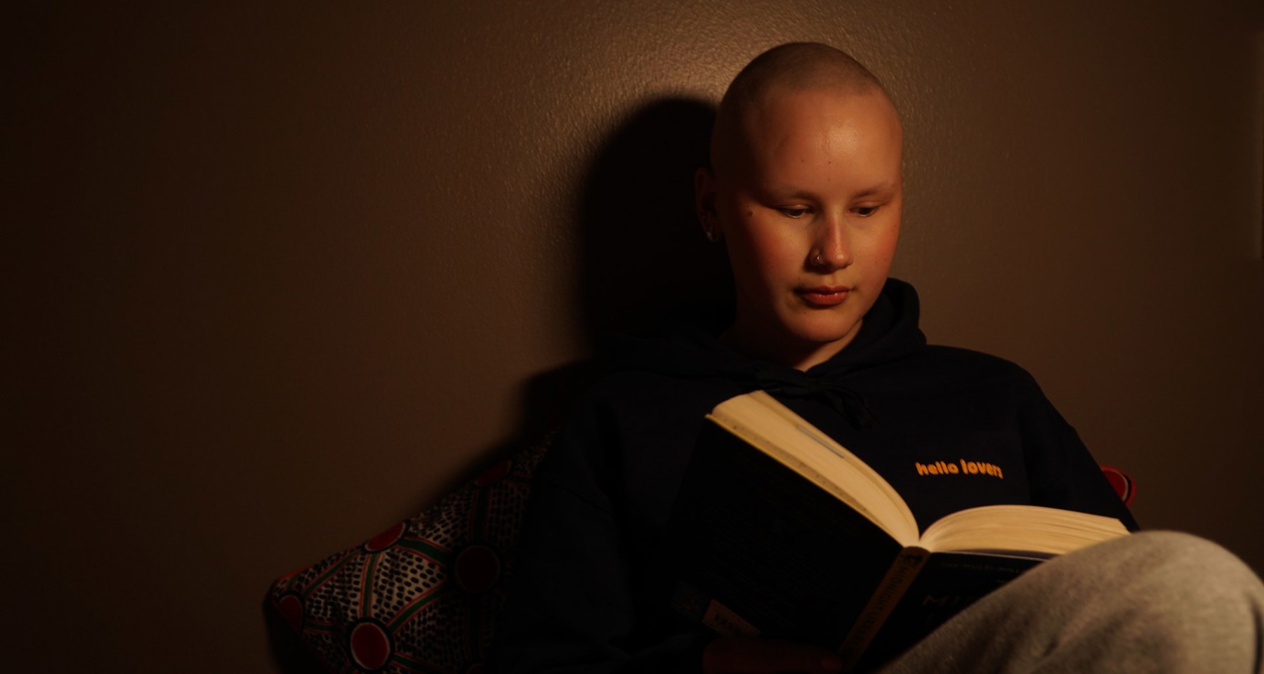 Ung kvinne uten hår leser en bok