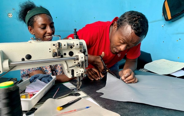 En ung kvinne og en mann sitter ved en symaskin og jobber. 