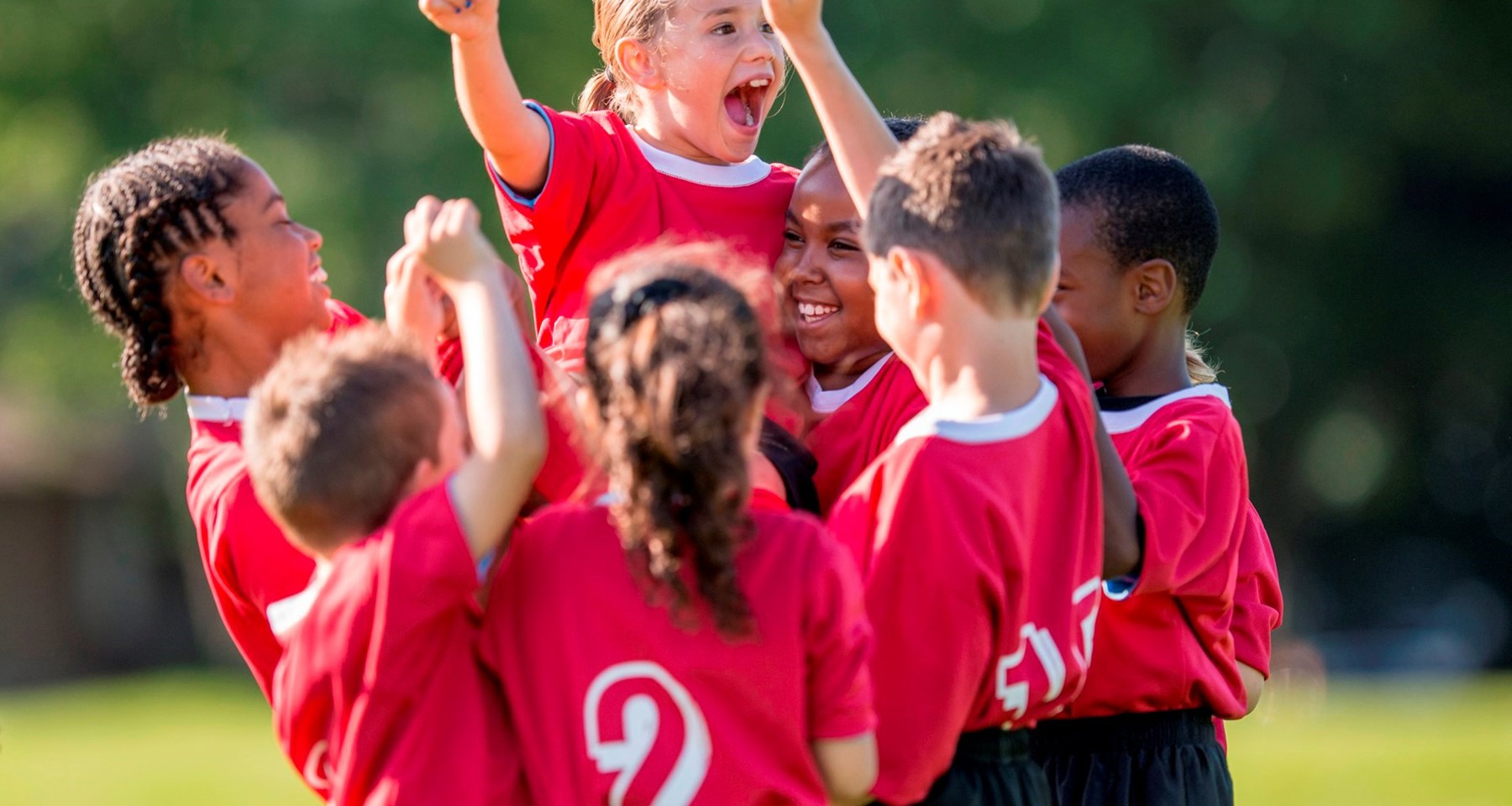En gruppe barn i fotballdrakter feirer og strekker hendene i været.