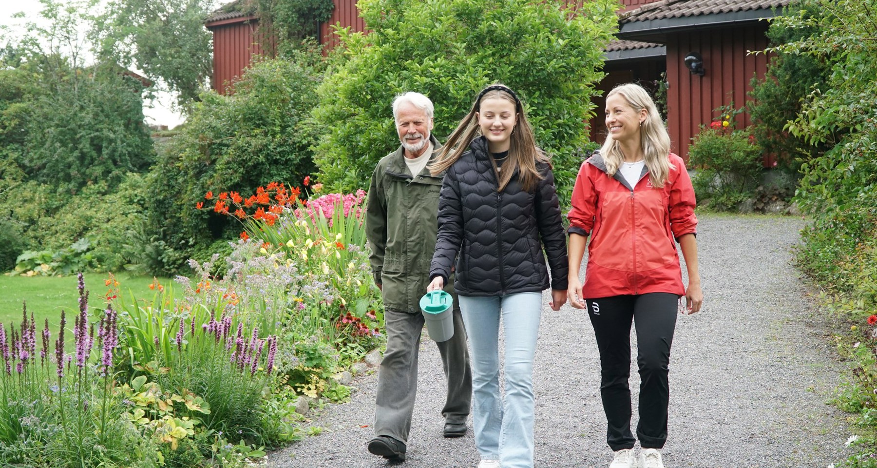 En morfar, en mor og en datter går i en oppkjørsel. Datteren holder en bøsse. Det er grønt og frodig rundt dem.