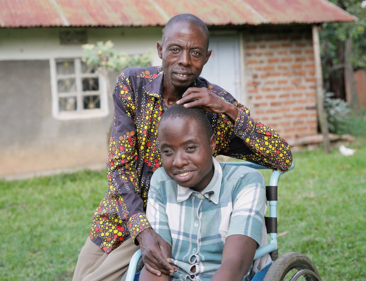 En mann sitter bak en ung gutt i rullestol.