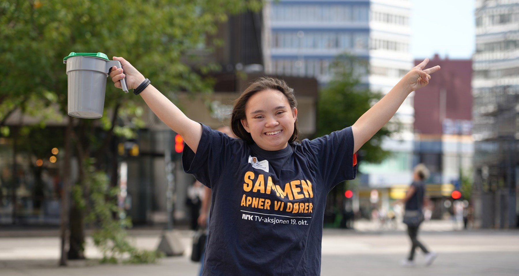 Smilende jente holder hendene i været og har en bøsse i den ene hånda. 