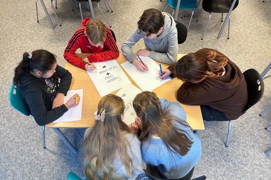 Seks barn sitter rundt en pult og tegner på plakater til TV-aksjonen