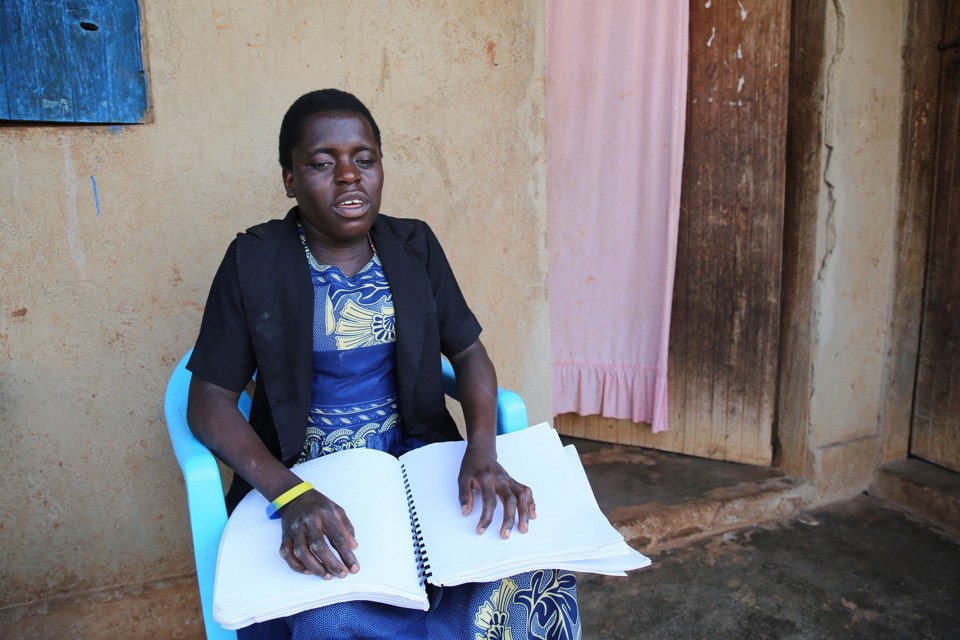 Jente sitter utenfor et hus og leser punktskrift.