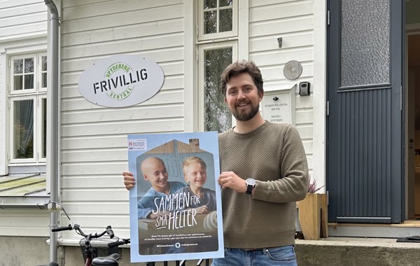Mann på utsiden av Spydeberg Frivilligsentral med plakat for TV-aksjonen 2024 i hendene