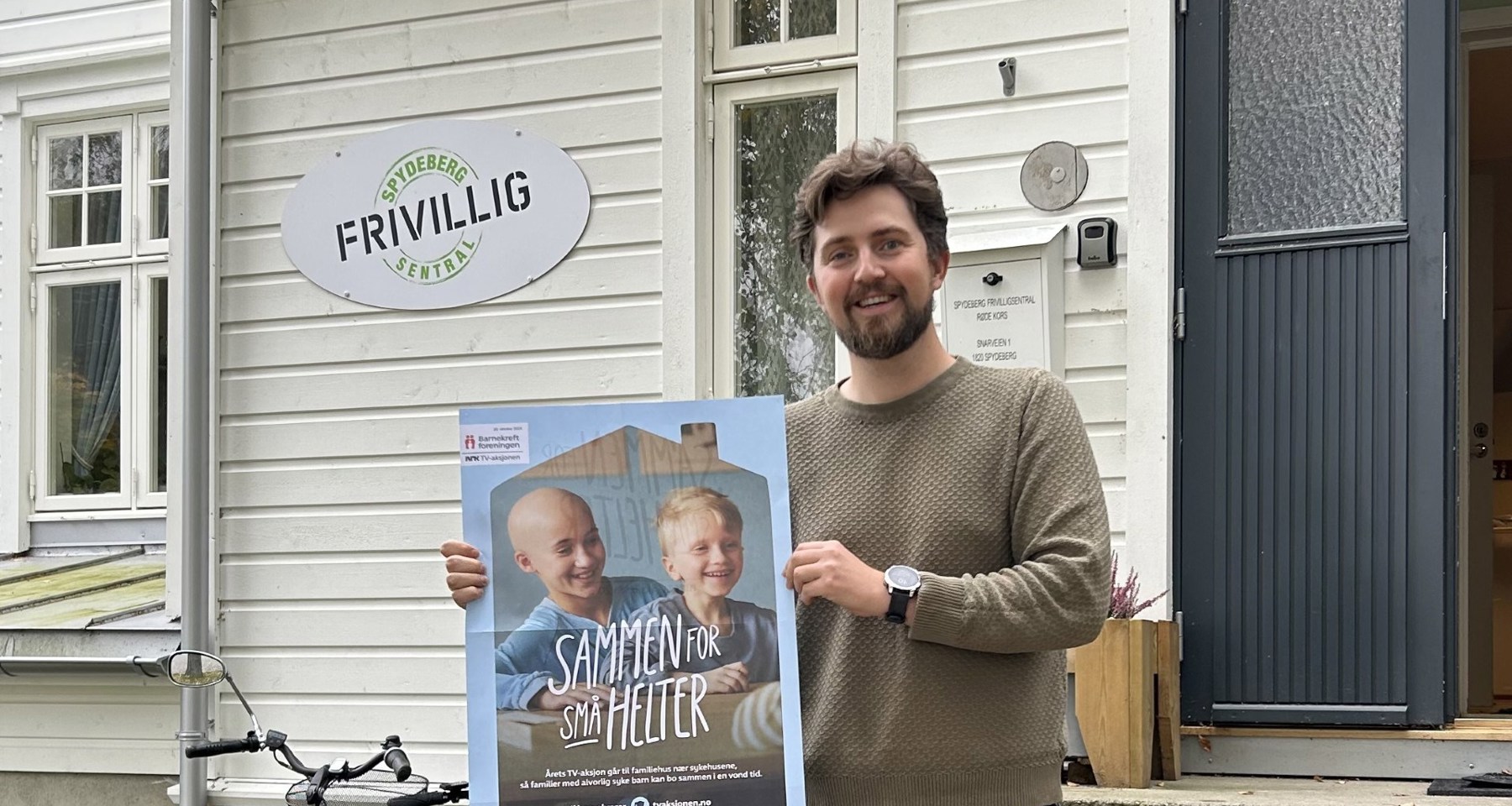 Mann på utsiden av Spydeberg Frivilligsentral med plakat for TV-aksjonen 2024 i hendene