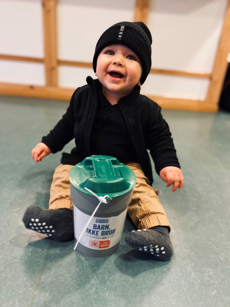 En liten gutt sitter på gulvet med en bøsse foran seg.