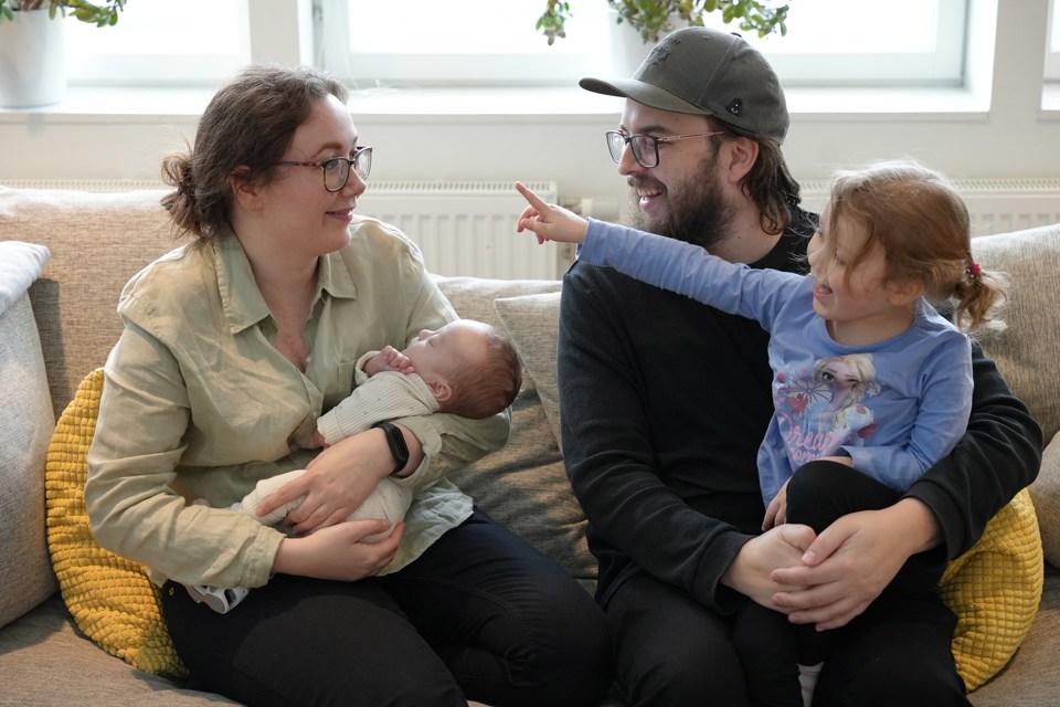 Familie på fire som sitter i en sofa, datter på fanget til far og mor holder en nyfødt baby.