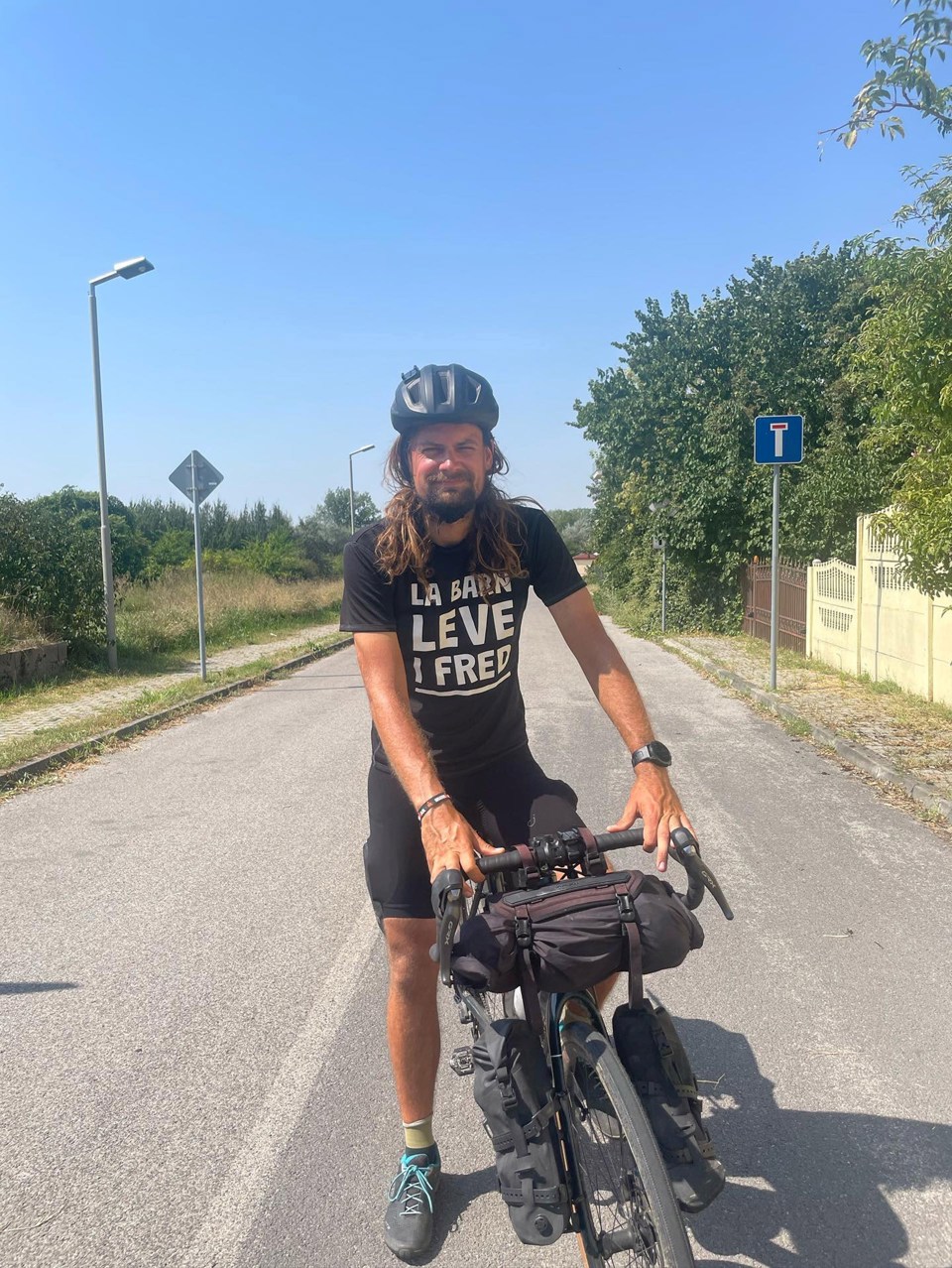 Mann på sykkel og TV-aksjonstskjorte. Han har skjegg og langt hår, og hjelm på.