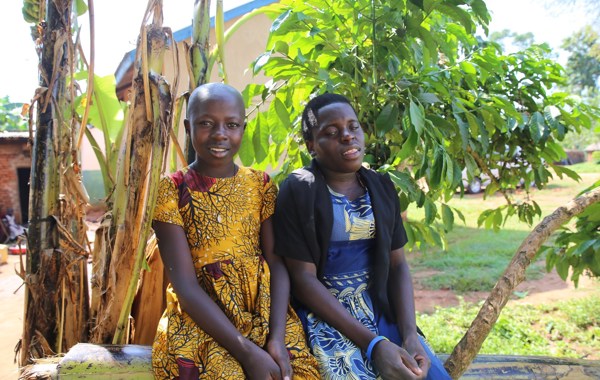 To unge jenter sitter på en trestamme ute i en frodig hage. 