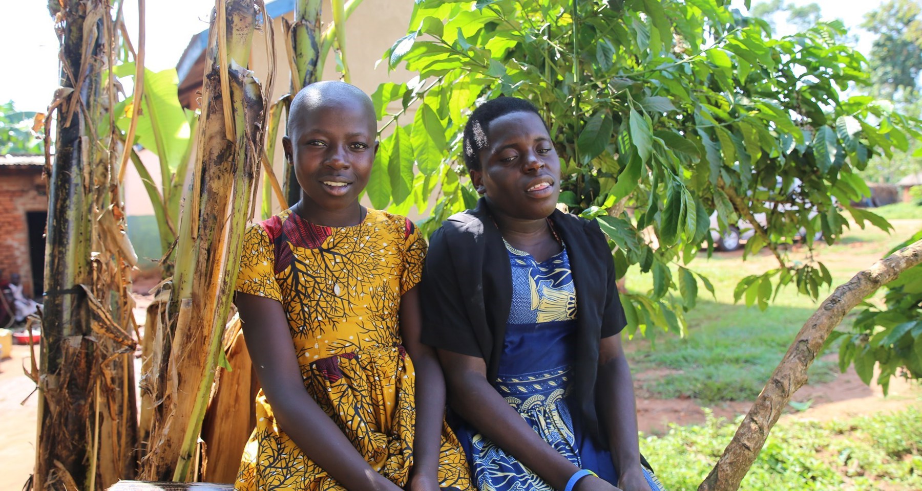 To unge jenter sitter på en trestamme ute i en frodig hage. 