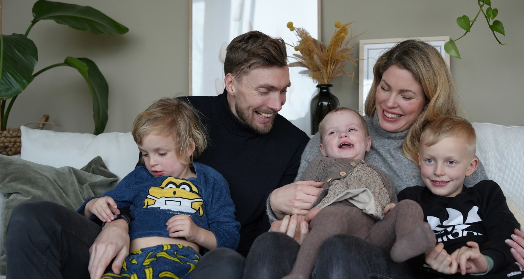 En familie på fem smiler og ler i en sofa.