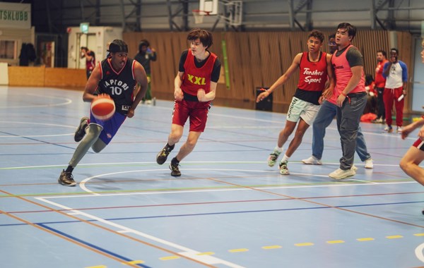En gruppe ungdommer spiller basketball i en gymsal.