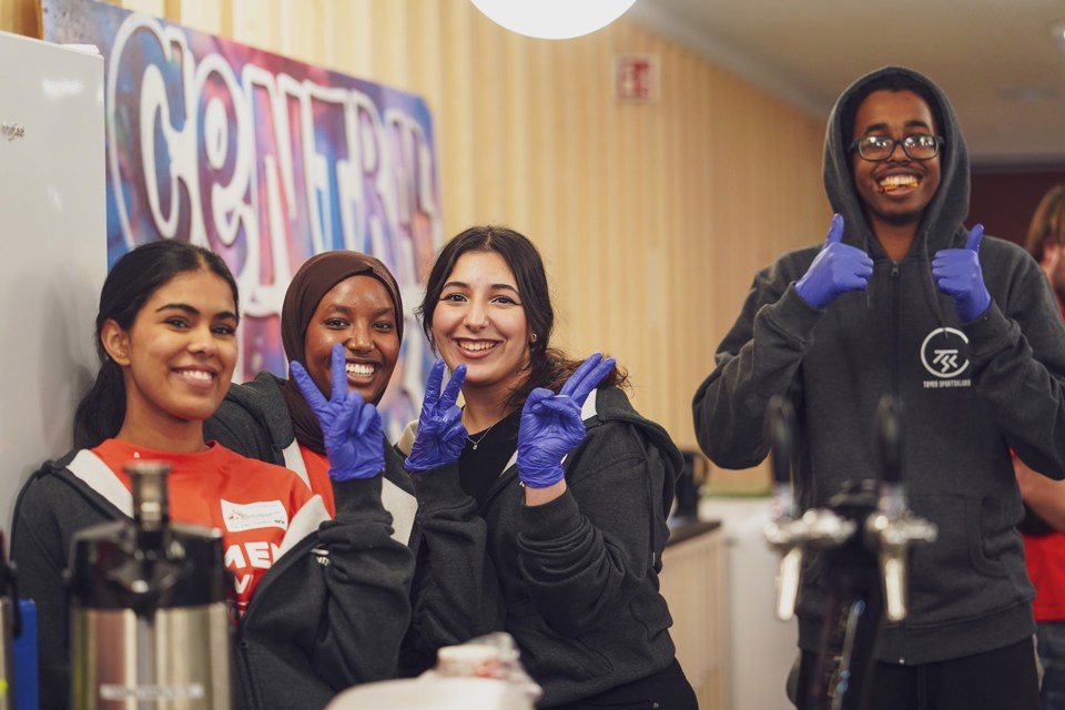 Fire ungdommer som smiler til kamera og viser tommel opp eller peacetegn. De har på seg engangshansker, og ser ut til å stå bak en disk.