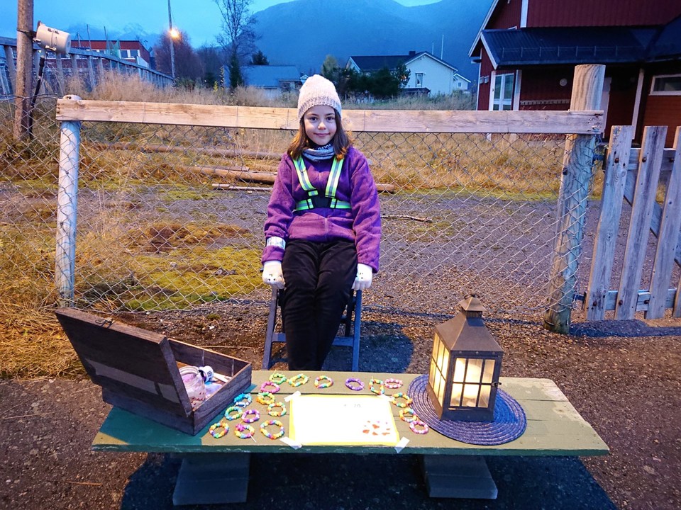 Ung jente sitter med ytterklær og refleks, og selger hjemmelagde armbånd.