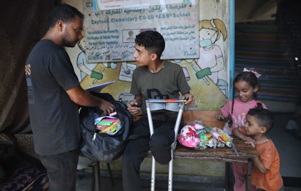 En gutt med amputert bein sitter på en benk. En voksen mann og to små barn står ved siden av. 