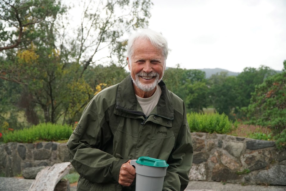 En eldre mann med skjegg iført grønn ytterjakke holder en bøsse i hånda.