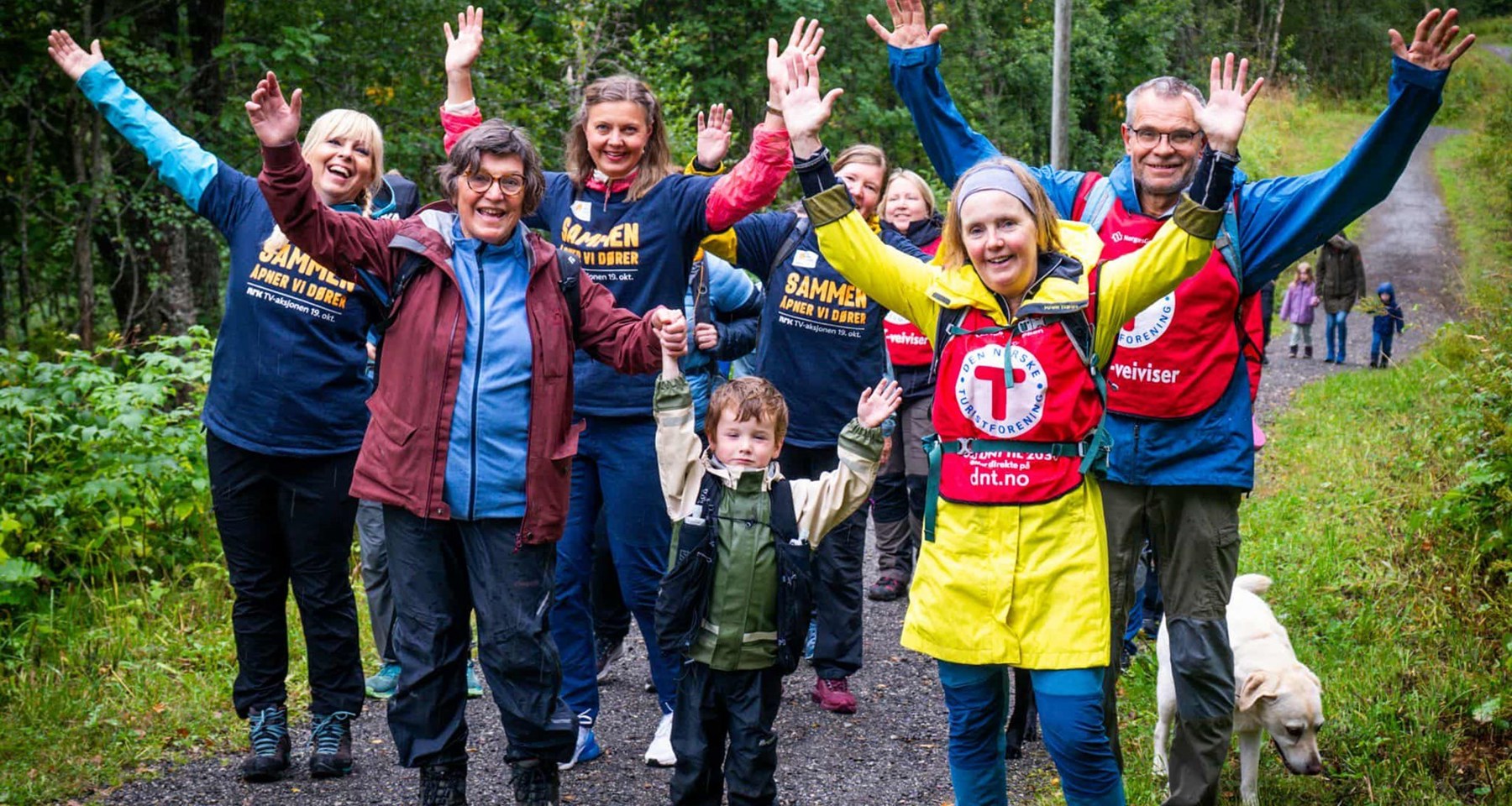 En gruppe mennesker er på tur og løfter armene mens de smiler. 