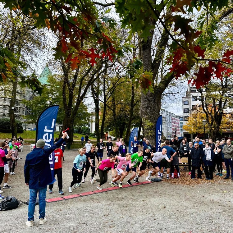 En rekke mennesker står på startstreken til en stafett. En mann står med horn i hånda som signaliserer start 