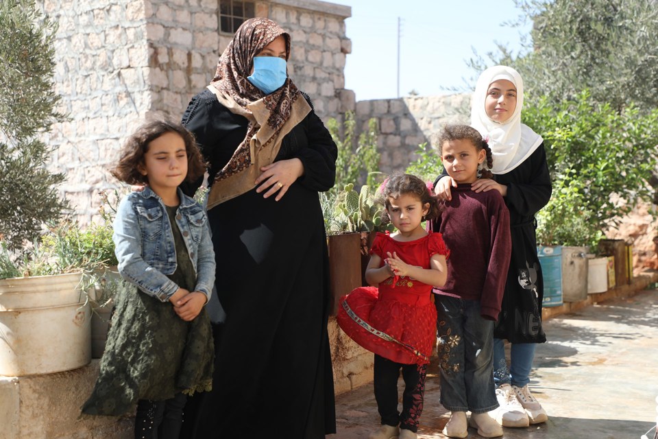En mor i hijab og med munnbind står sammen med fire døtre. En av døtrene har hijab.