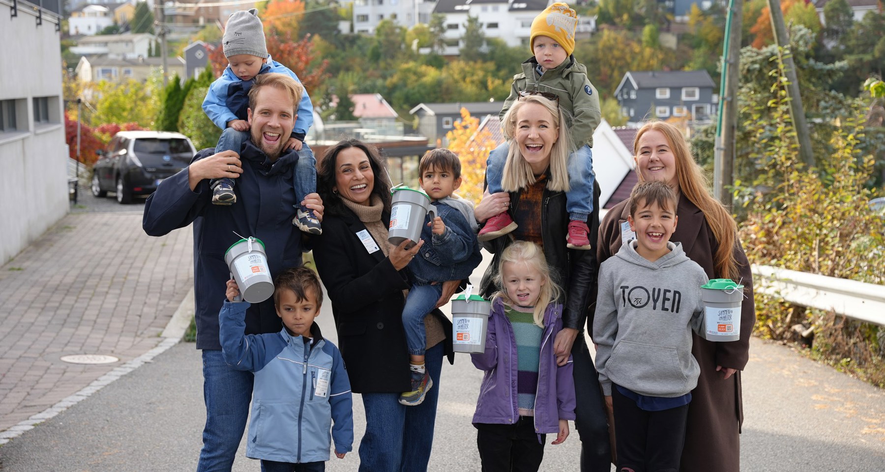 Fire voksne og seks barn smilende med bøsser i henda.