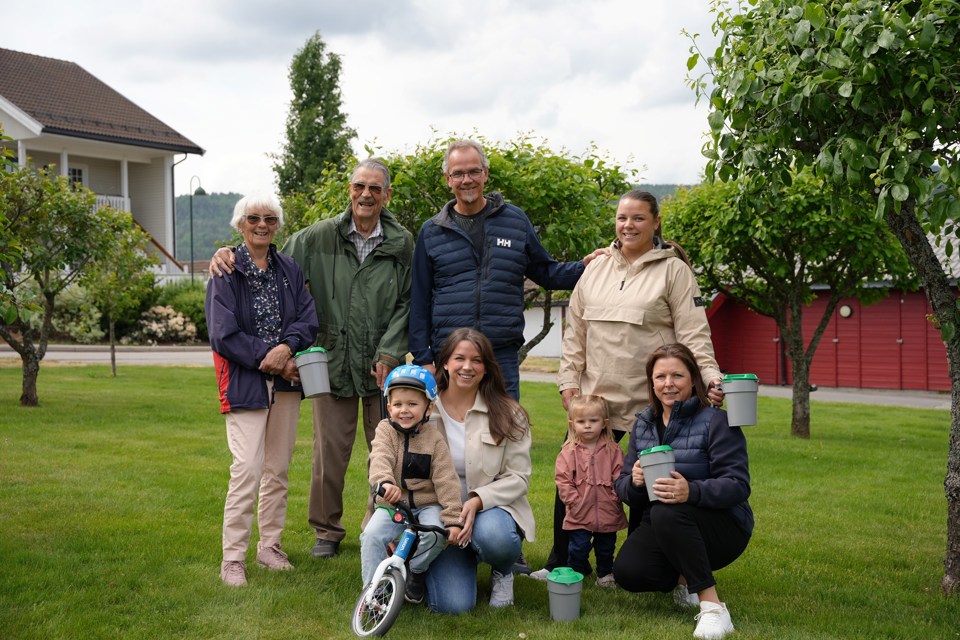 En familie med voksne og barn står i en hage med bøsser i hendene. 