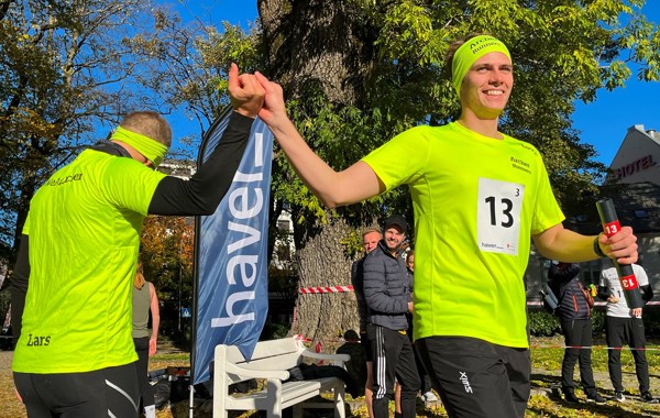 To menn i neongule tskjorter holder hverandre i hendene hevet, en med stafettpinne i hånden 