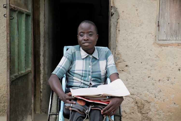 Gutt sitter i rullestol med skolebøker i fanget.