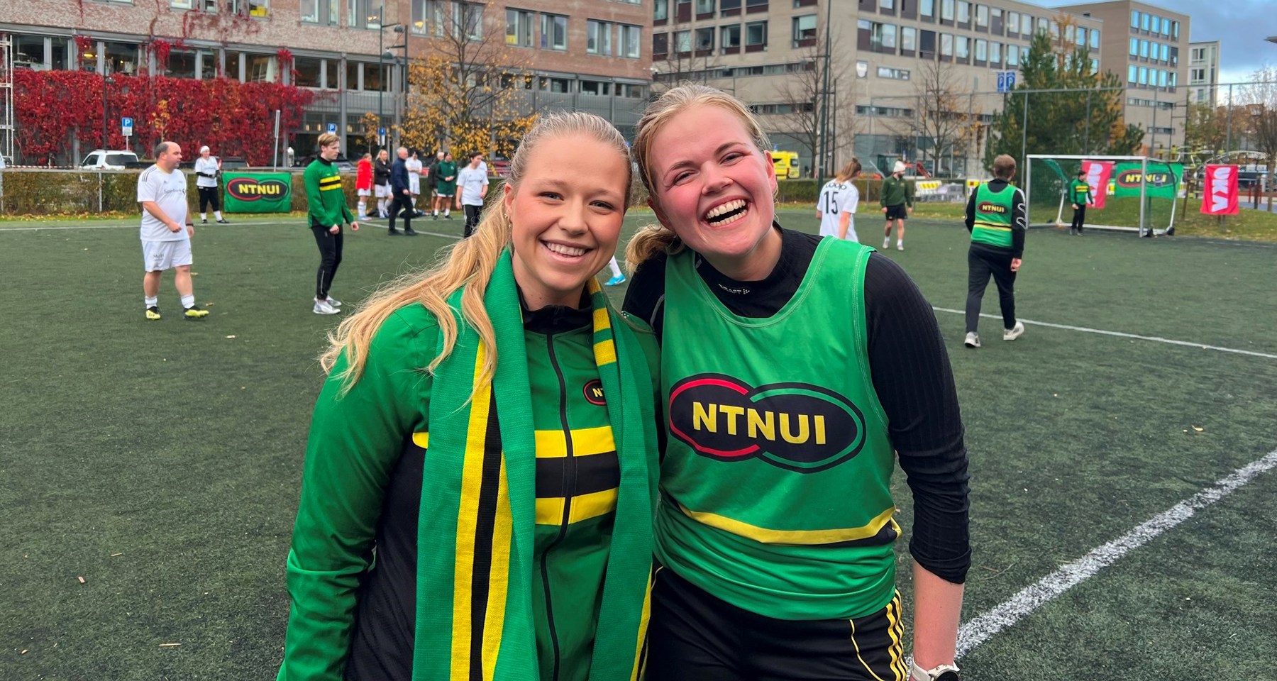 To jenter står på en fotballbane med grønne drakter og smiler. 