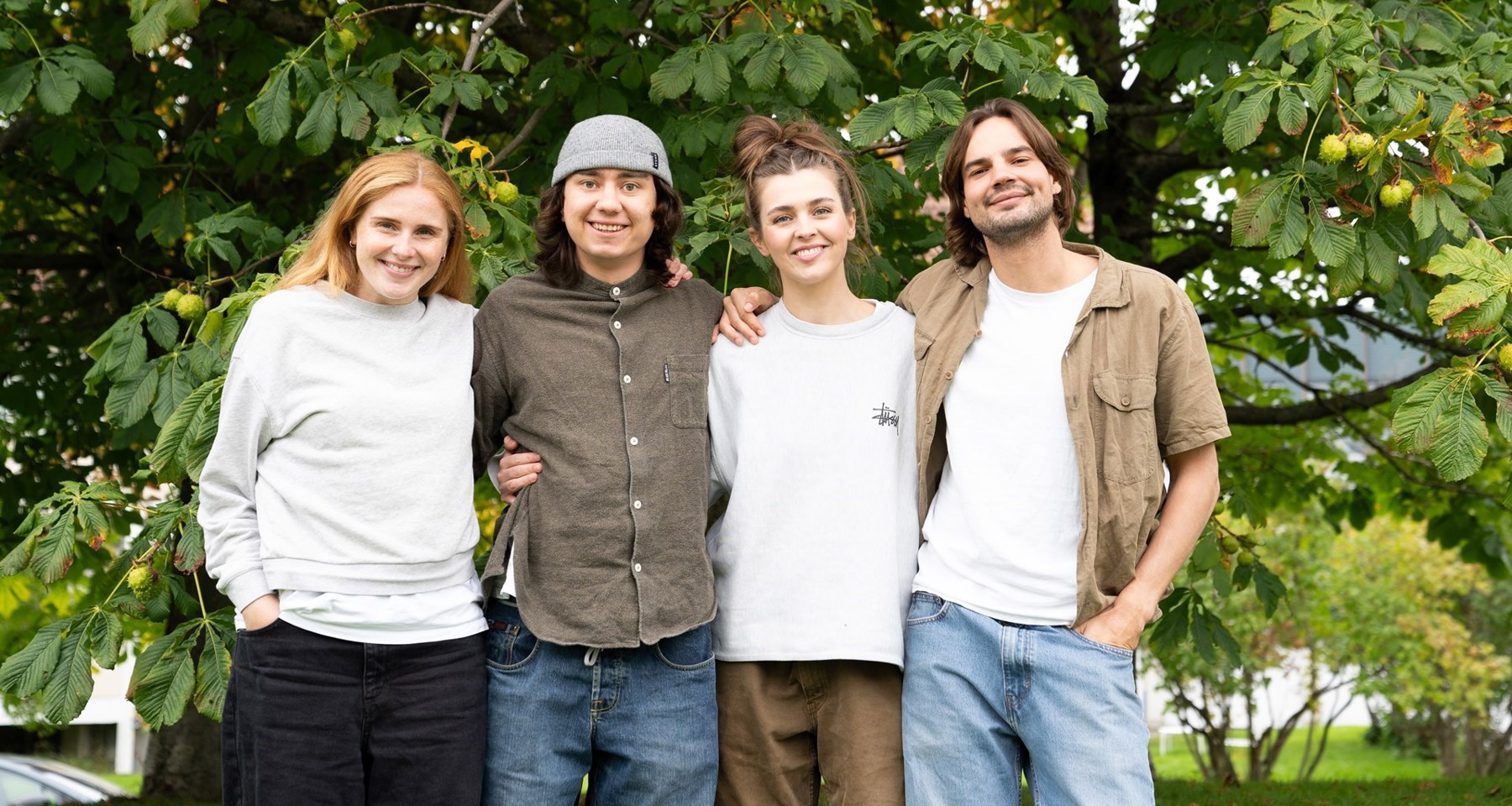 To kvinner og to menn som holder rundt hverandre og står foran et stort, grønt tre