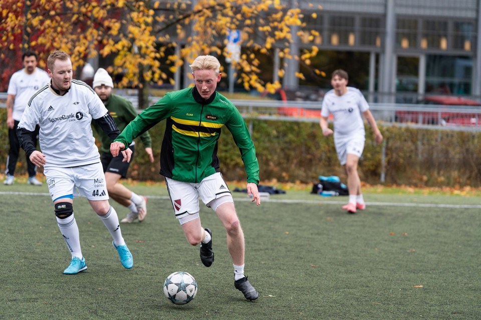 Unge menn spiller fotball i hvite og grønne trøyer.