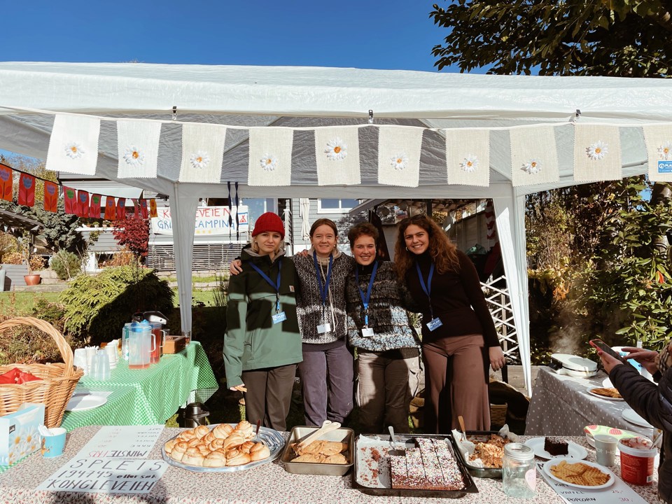Fire jenter som står i et telt, med kaker og vafler på bord foran dem. De har kakesalg for TV-aksjonen. Det er pent gjort med duker og pynt.