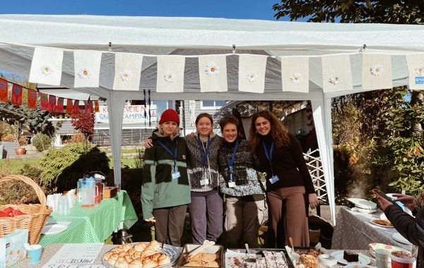 Fire jenter som står i et telt, med kaker og vafler på bord foran dem. De har kakesalg for TV-aksjonen. Det er pent gjort med duker og pynt.