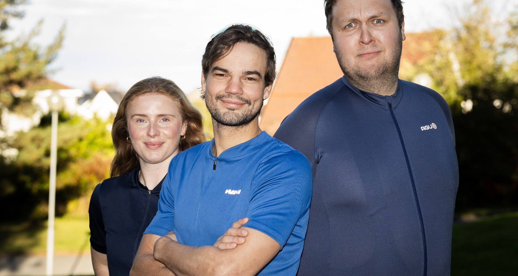 To menn og en kvinne i treningsklær smiler til kamera.