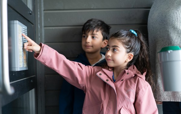 To barn ringer på en dør, mens en voksen står bak og holder en bøsse.