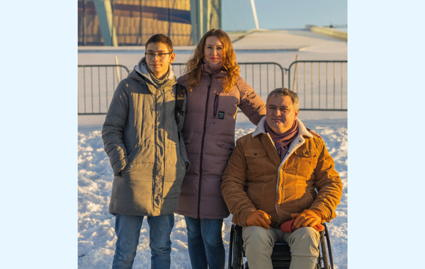 En mann sitter i rullestol foran operaen i Oslo en vinterdag. Ved siden av står en kvinne og en gutt på 16 år. 