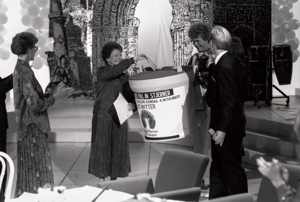 Gro Harlem Brundtland i studio i 1990, gir gave til TV-aksjonen på vegne av regjeringen. Hun putter en sjekk i en stor bøsse, og får applaus av folk rundt.