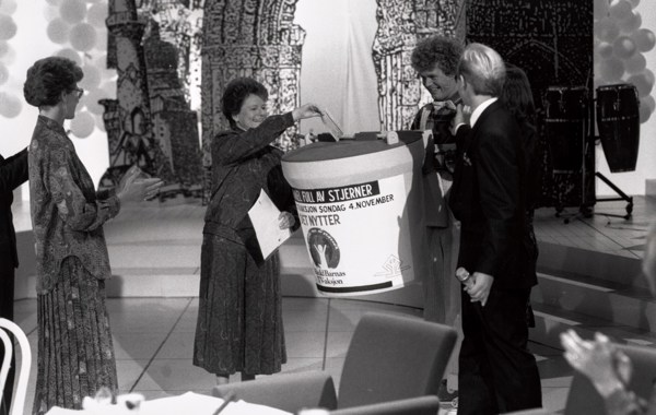 Gro Harlem Brundtland i studio i 1990, gir gave til TV-aksjonen på vegne av regjeringen. Hun putter en sjekk i en stor bøsse, og får applaus av folk rundt.